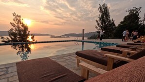Un espace aménagé au bord de la piscine, avec des chaises longues et une vue sur le coucher de soleil se reflétant sur l’eau.