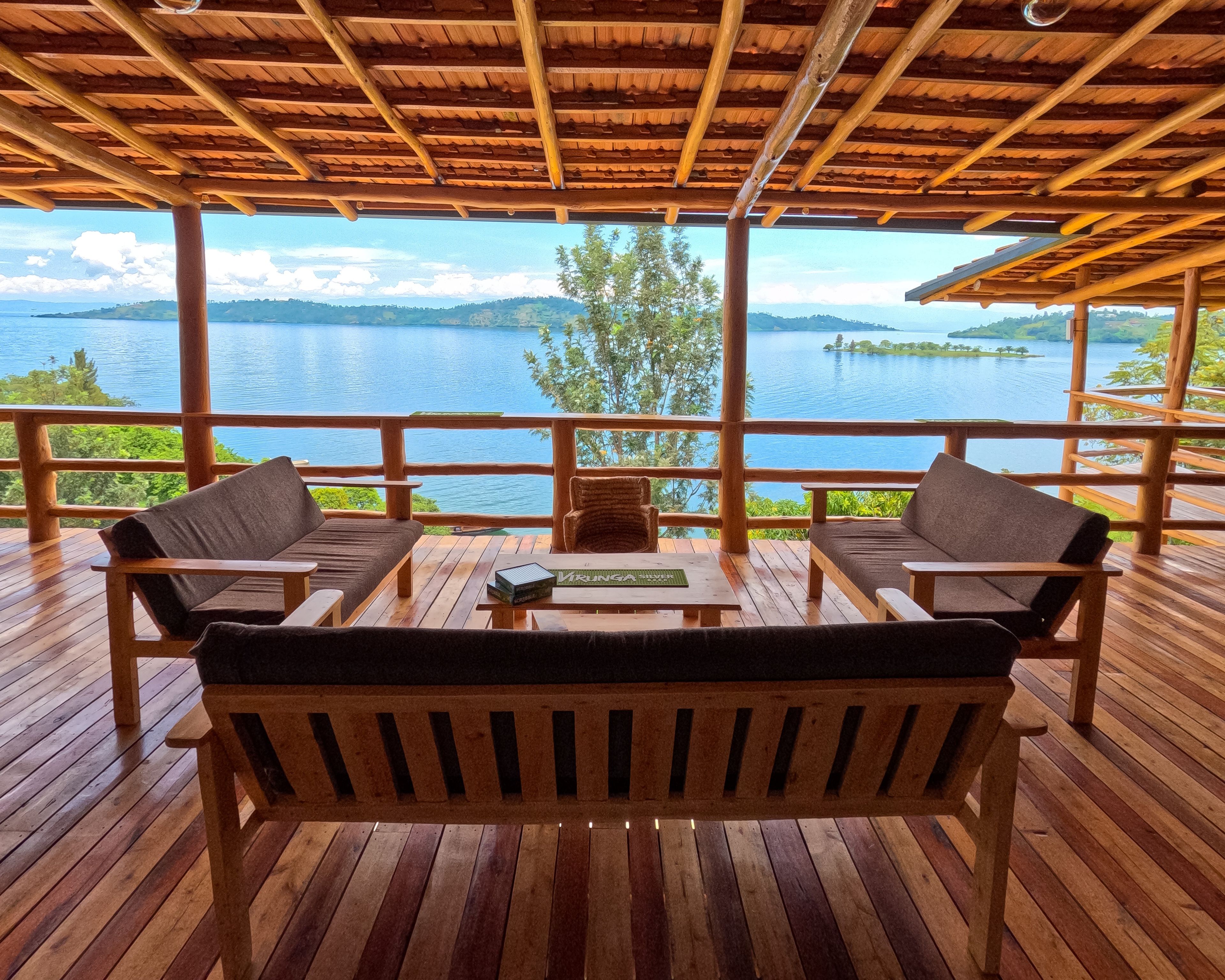 A wooden deck with two sofas and a table, overlooking a lake with a distant island.