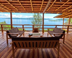 A wooden deck with two sofas and a table, overlooking a lake with a distant island. - Umutuzo Lodge Kivu Lake (Boneza)