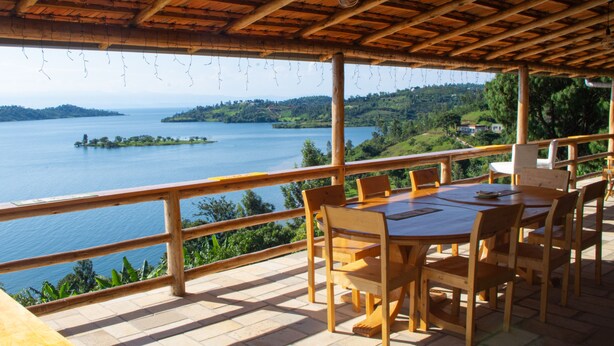 Un espace de restauration en plein air avec une table et des chaises en bois, offrant une vue sur un lac et la verdure environnante.