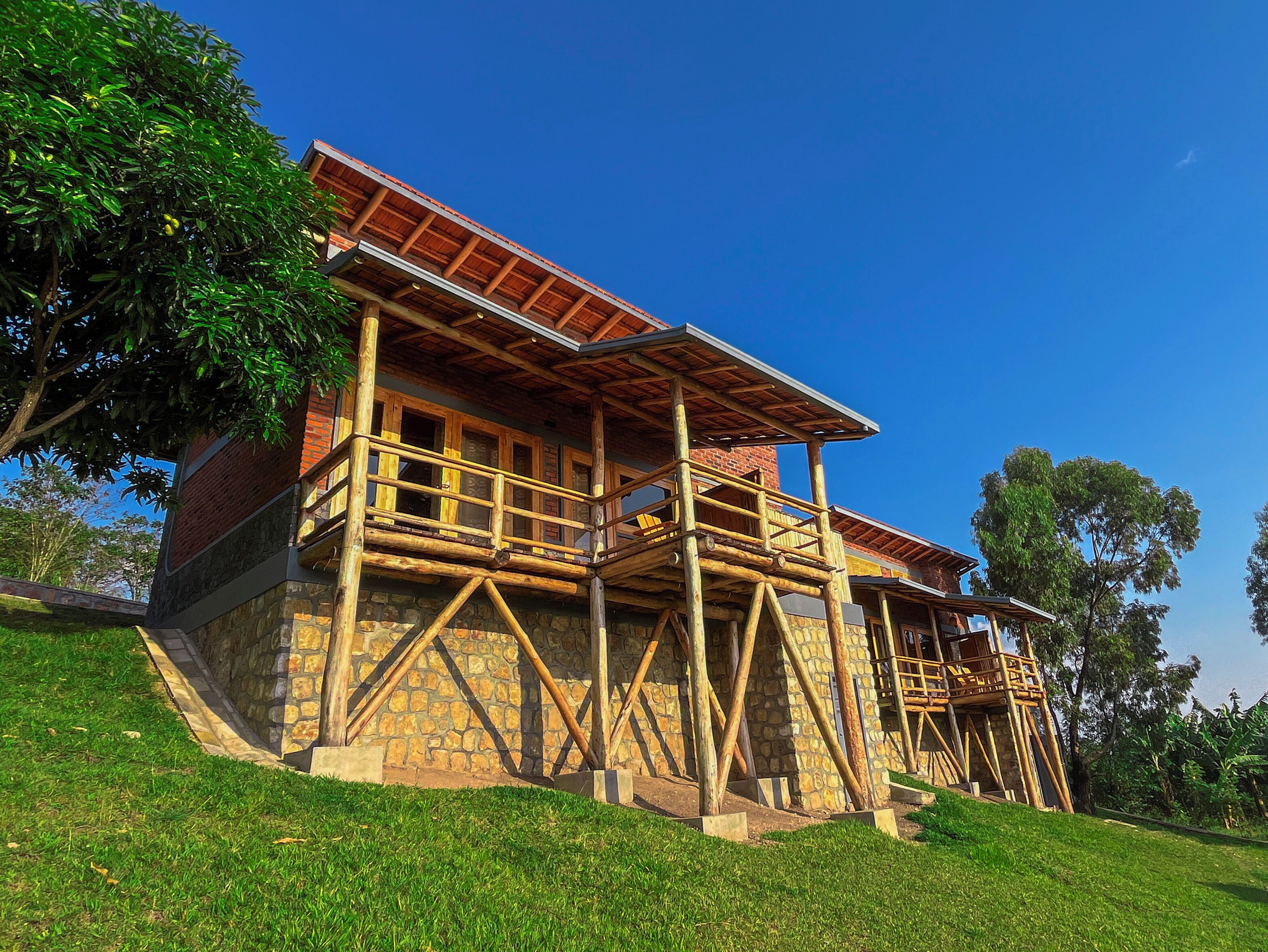 A two-story wooden house with a stone foundation, a balcony, and a red roof.