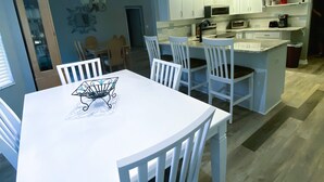 Une cuisine moderne avec des meubles blancs, un îlot central et un coin repas comprenant une table et des chaises blanches.