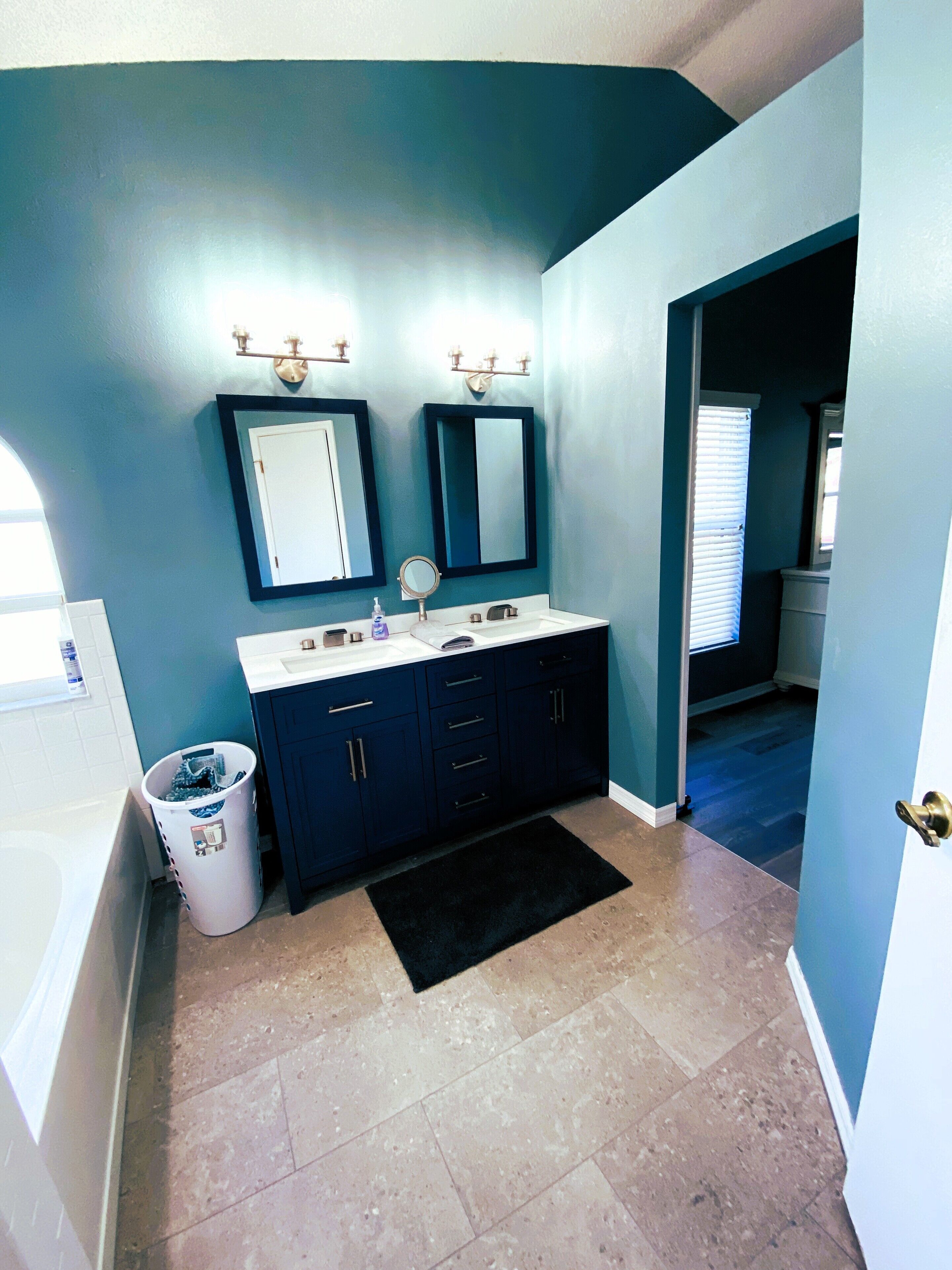 A bathroom with two sinks, dark blue walls, and a black rug.