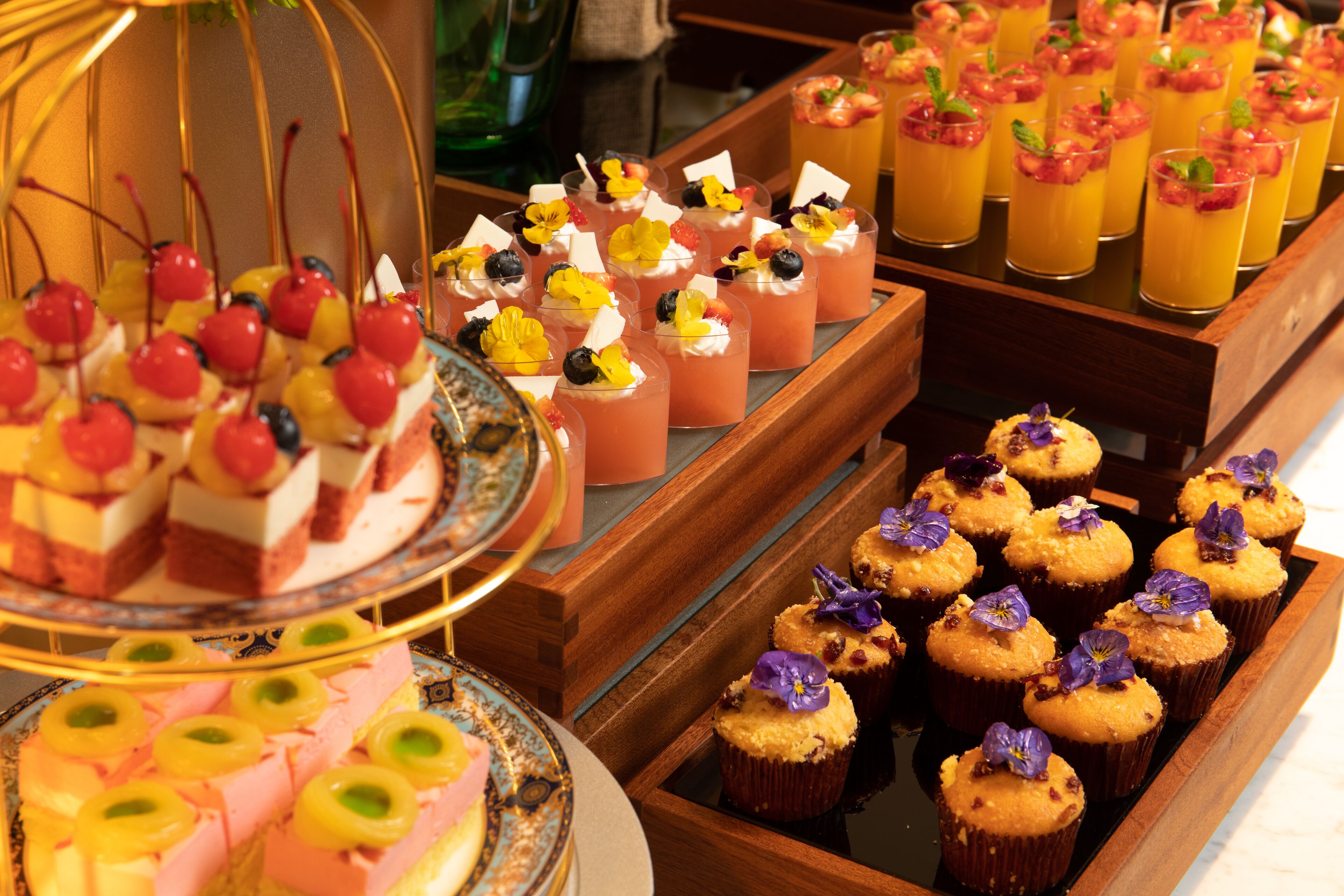 A variety of desserts including cupcakes and fruit-based drinks, arranged on trays and a stand.
