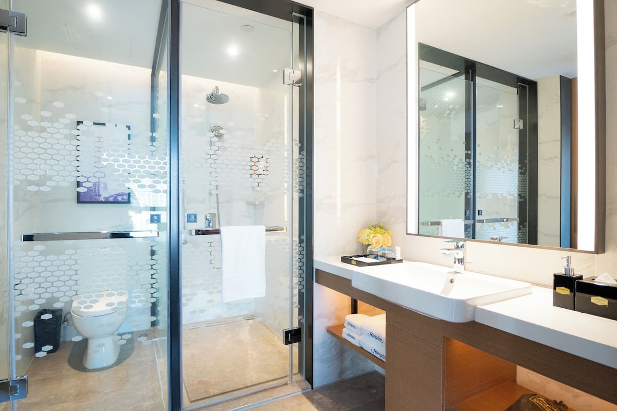 A modern bathroom with a glass-enclosed shower, a large mirror, and a white sink.