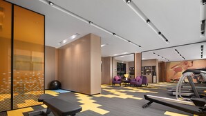 A modern hotel gym with exercise equipment, a seating area, and a large mirror.