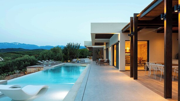 Un área de piscina moderna al aire libre con sillones de descanso y comedor, con vistas a un paisaje montañoso.