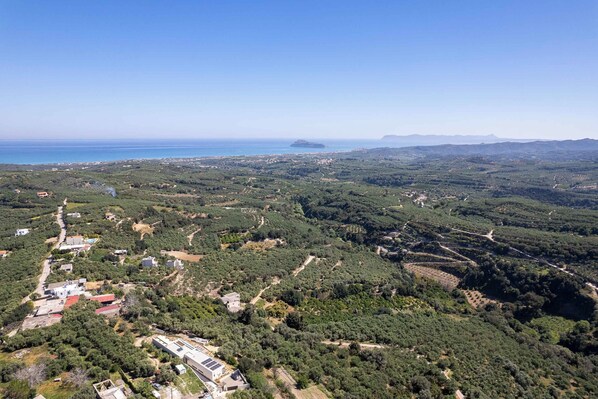 An aerial view of a coastal area with terraced fields, a few buildings, and a distant island.