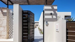 Entrada de un edificio moderno con una reja negra, un muro de piedra y un cielo azul despejado.