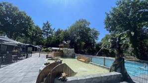 Un espace piscine agrémenté d’un mur en pierre, de bancs en bois et d’un arbre.