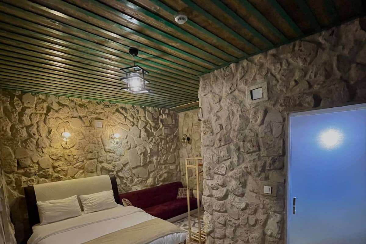 A bedroom with a stone wall, a bed, a red sofa, and a wardrobe.