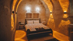 A stone-walled bedroom with a bed, two wall-mounted lights, and a nightstand. - Daphne Cave Cappadocia (Avanos)