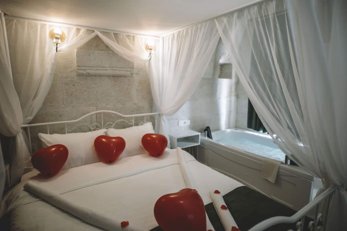 A bed with white linens, heart-shaped pillows, and a canopy.