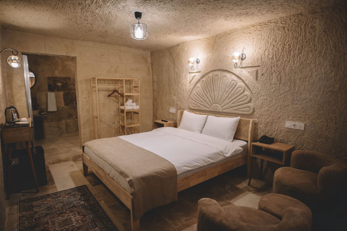 A bedroom with a wooden bed, a bedside table, a chair, a wardrobe, and a mirror.