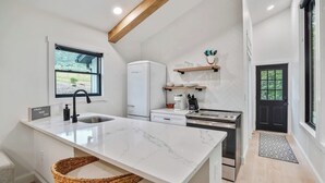 A modern kitchen with a marble island, a built-in refrigerator, and a black door. - Luxury Hocking Couples Cabin | Secluded! Hot Tub! (Logan)