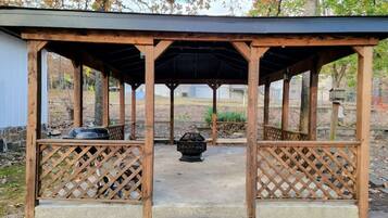 A wooden gazebo with lattice railings, a central fire pit, and a concrete floor.