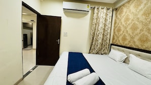 Une chambre d’hôtel avec un lit, une fenêtre avec des rideaux, un appareil de climatisation et une porte donnant sur un couloir.