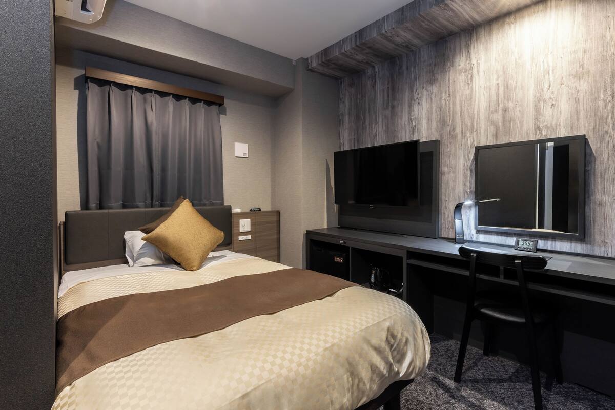 Una habitación de hotel con una cama, un escritorio, un televisor y un espejo.