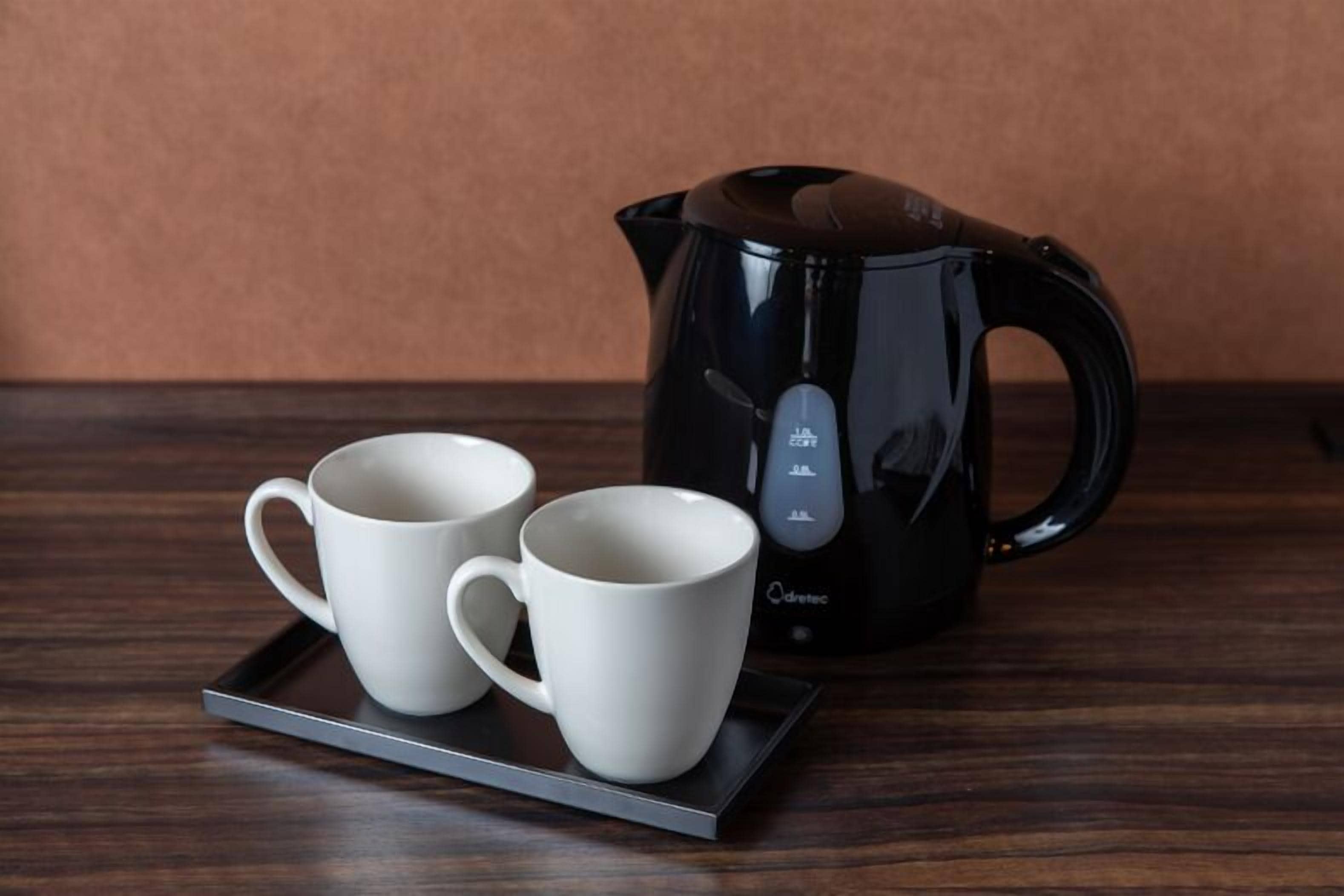A black electric kettle and two white mugs on a tray.