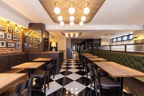 Un restaurant avec un sol à carreaux, des tables en bois et des banquettes recouvertes d’un tissu vert.