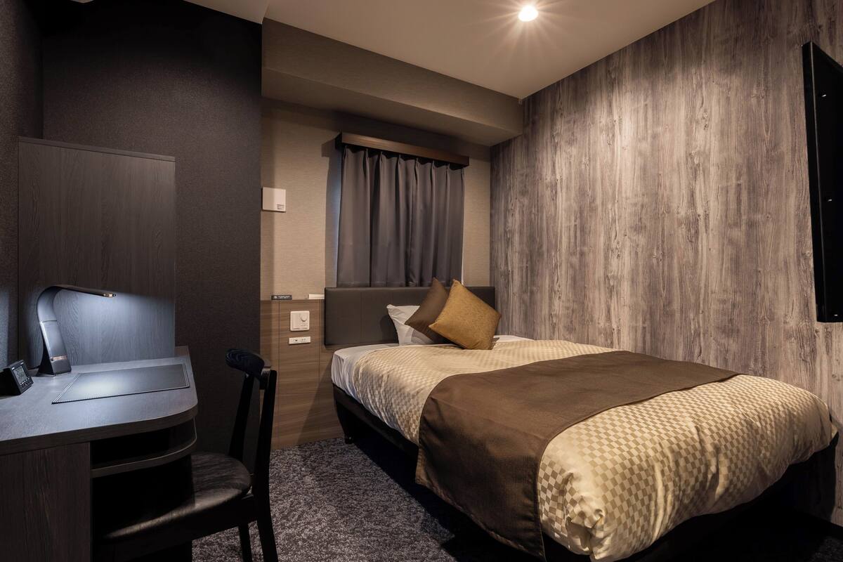 Una habitación de hotel moderna con escritorio, silla y una cama grande con una manta marrón.