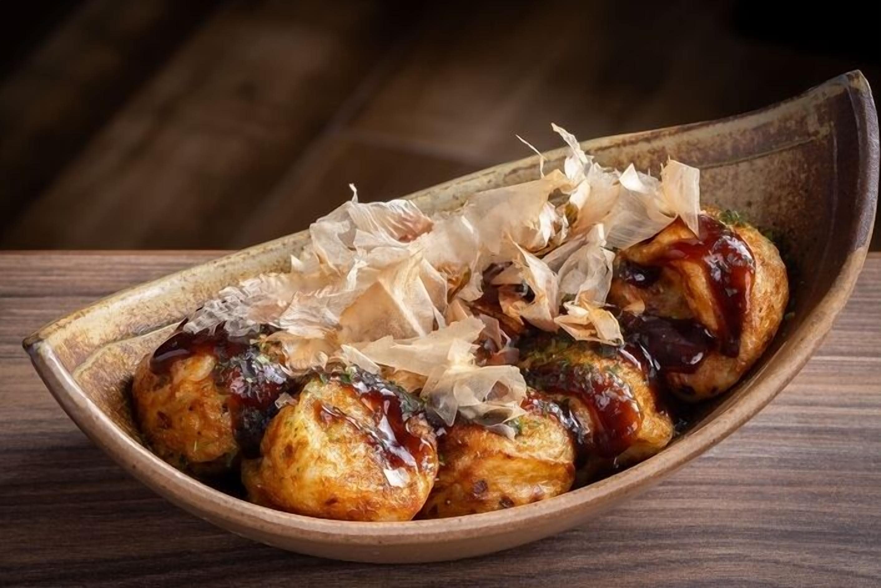 A wooden bowl containing grilled chicken pieces with a glaze, garnished with shredded daikon radish and green herbs.