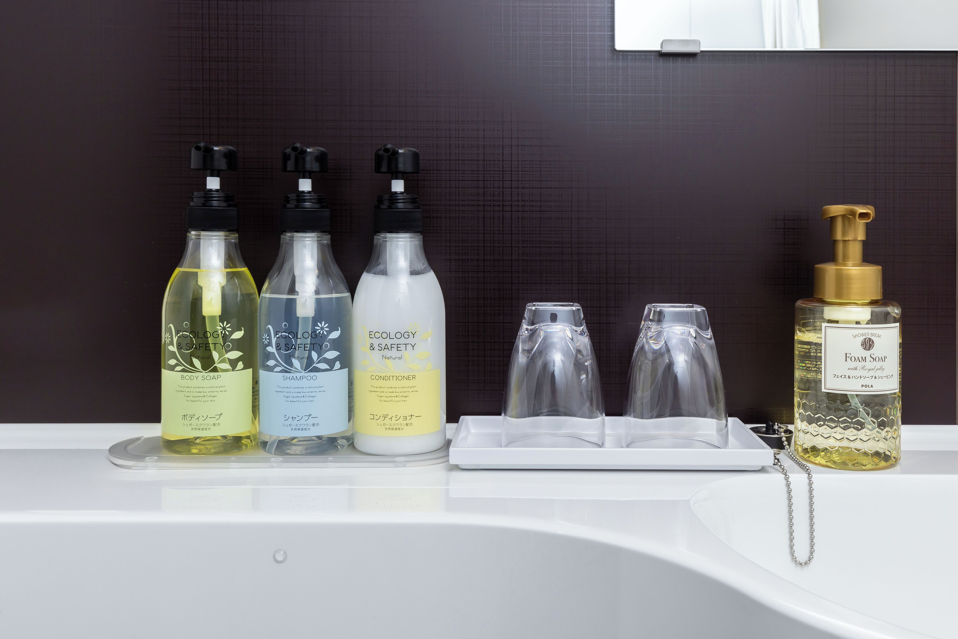 A bathroom with a white sink, three bottles of liquid soap, and a bottle of foam soap.