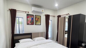 A bedroom with a large bed, a wardrobe, an air conditioning unit, and two paintings on the wall. - PICHAPON  RESORT (Pak Chong)