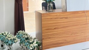 A reception area with a wooden desk, a vase of flowers, and two framed pictures on the wall. - PICHAPON  RESORT (Pak Chong)