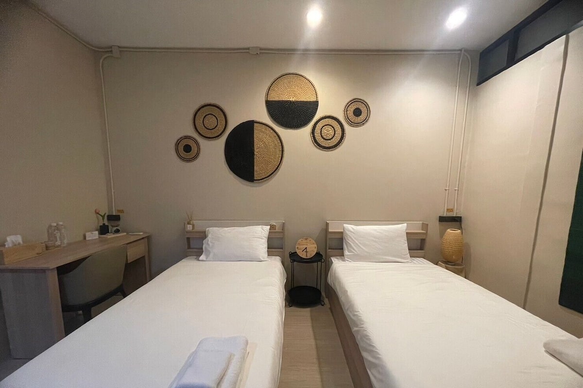 A hotel room with two single beds, a desk, and a wall decorated with circular woven art pieces.