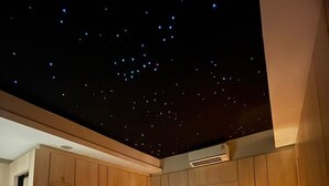 Ein Schlafzimmer mit Sternenhimmel-Decke, Holzwänden, einem Bett mit weißen Leinen und einer Nachttischlampe.