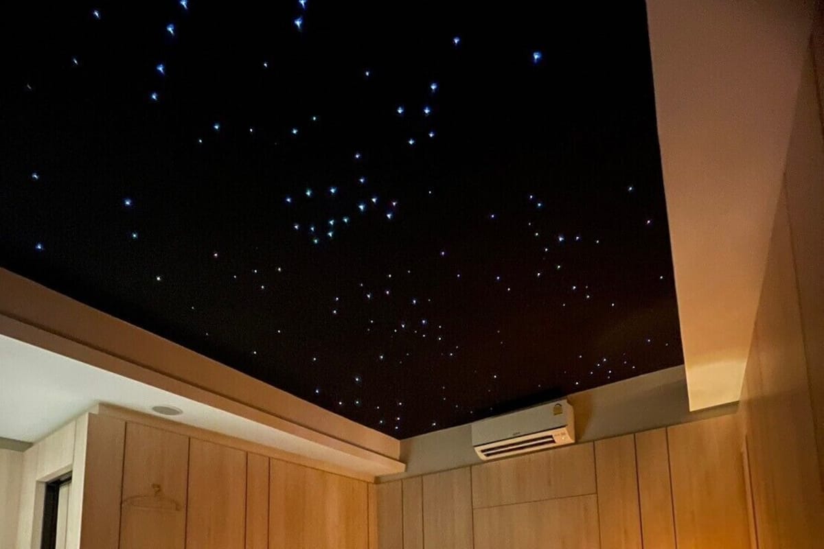 A bedroom with a starry sky ceiling, wooden walls, a bed with white linens, and a bedside lamp.