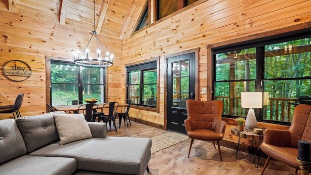 A cozy cabin interior with a wooden interior, a dining area, and large windows offering a view of the forest.