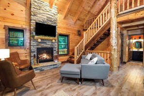 Cozy cabin interior with a stone fireplace, comfortable sofa, and wooden staircase.
