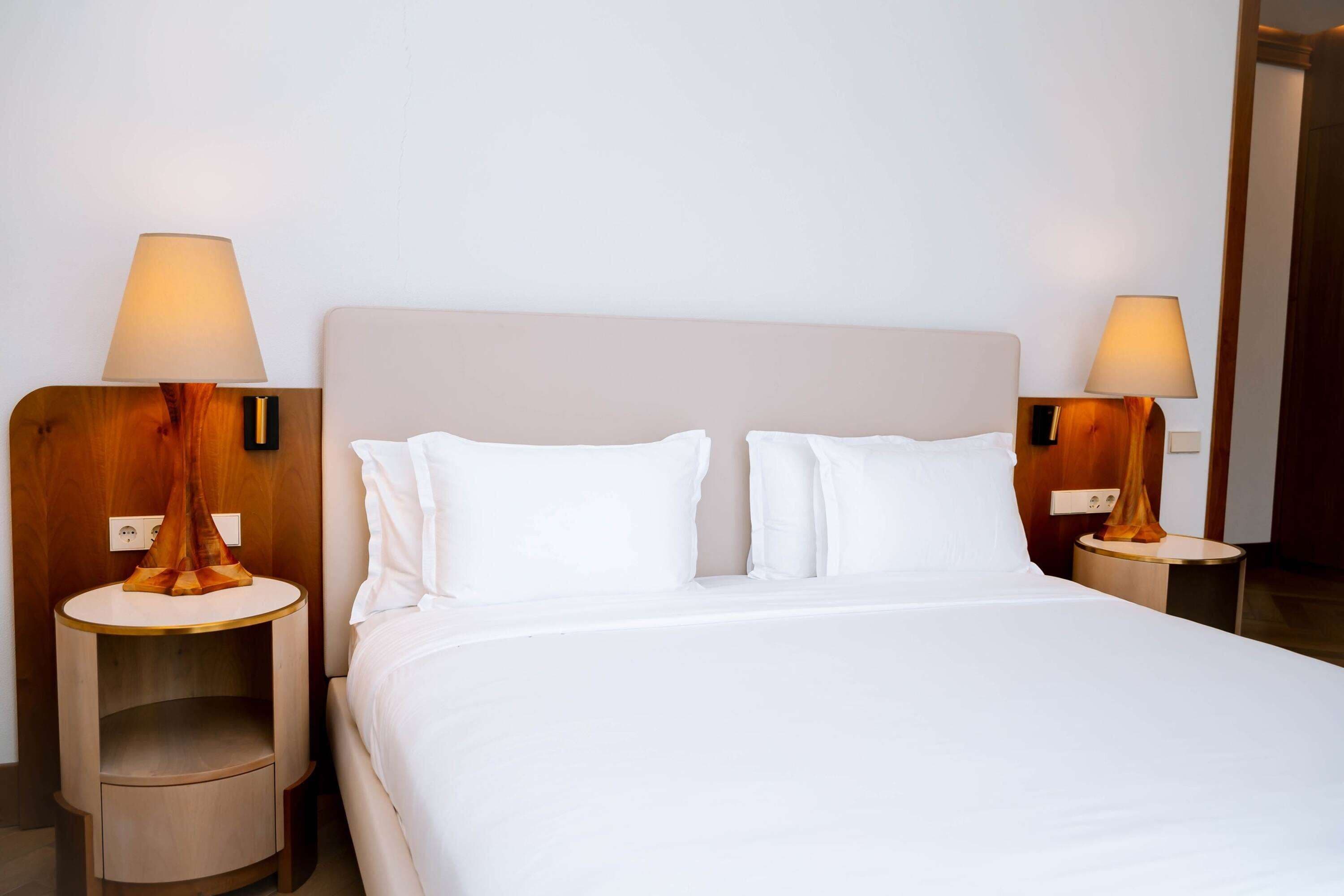 Una habitación de hotel con una cama grande, dos mesitas de noche con lámparas y una decoración en tonos neutros.