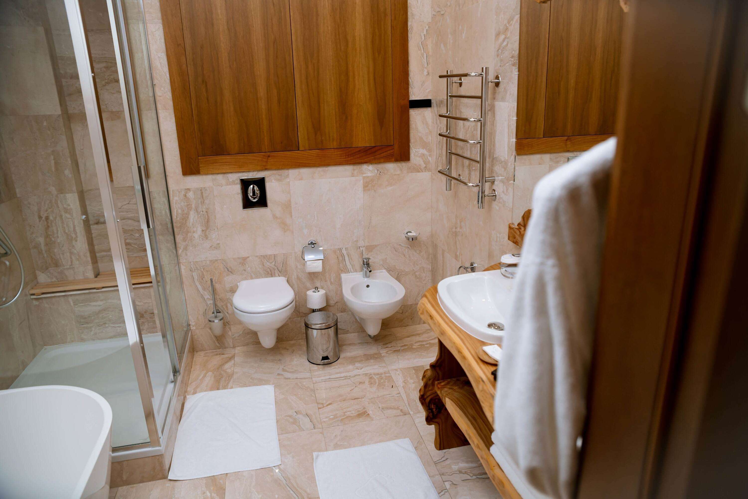 A modern bathroom with a glass shower enclosure, a toilet, bidet, and a sink with a wooden vanity.