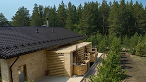 En stuga byggd av trä med ett tak täckt av takpannor, en bastu och en terrass som omges av träd.