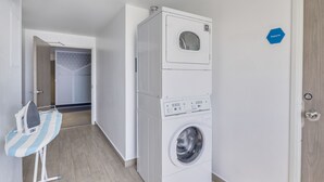 A compact laundry room with a front-loading washing machine, a drying machine, and an ironing station. - One Morelia Acueducto (Morelia)