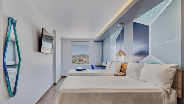 A modern hotel room with a large bed, a desk, and a view of a cityscape. - One Morelia Acueducto (Morelia)