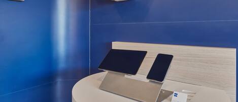Um display moderno com dois laptops numa plataforma circular, com uma parede azul e prateleiras geométricas ao fundo.