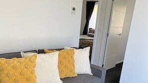 A grey sofa with yellow and white cushions, a wooden side table, and a carpeted floor.