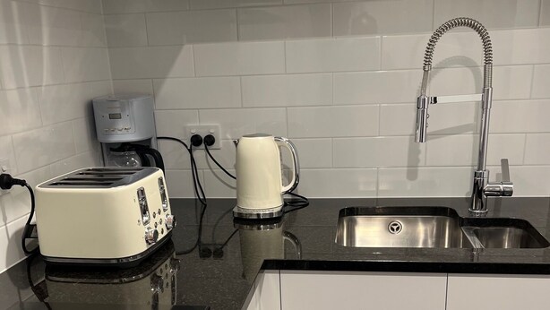 A modern kitchen with white cabinets, a black countertop, a stainless steel sink, a coffee maker, and a toaster.