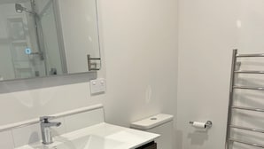 A modern bathroom with a white sink, dark wood vanity, a toilet, and a glass shower enclosure.
