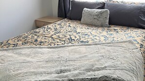 A bed with a floral-patterned bedspread, a grey throw blanket, and a grey pillow.