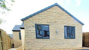 A stone house with a pitched roof and two windows with shutters.
