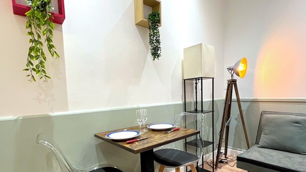 Un coin repas avec une table dressée pour deux personnes, deux chaises, une lampe et un canapé.