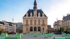Un bâtiment historique doté d’une tour horlogée, de grandes fenêtres et d’une cour intérieure avec des bancs verts.