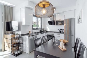 A modern kitchen with stainless steel appliances, a dining area with a dark wooden table, and a unique spherical pendant light.