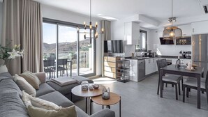 Un apartamento moderno con sala de estar, comedor, cocina y grandes puertas de vidrio correderas que dan a un balcón con vistas a la montaña.