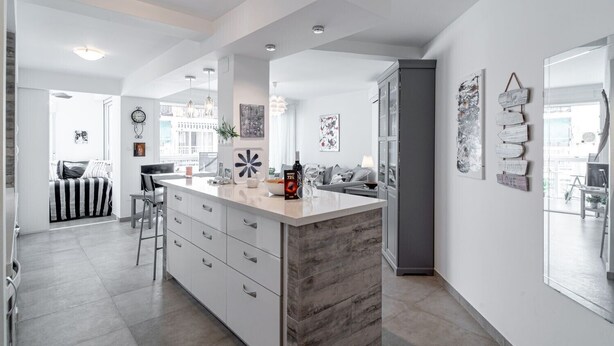 A modern kitchen with a central island, white cabinetry, and a view to the living area.